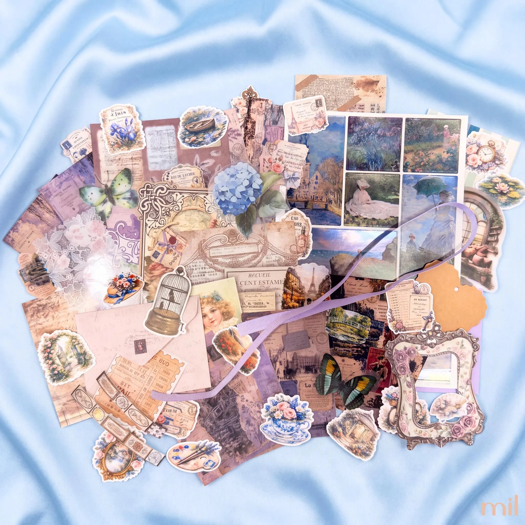 A collection of vintage-style decorative stickers and ephemera arranged in a fan shape on a light blue satin fabric background. The stickers feature illustrations of blue hydrangeas, butterflies, old photographs, postcards, envelopes, and frames.