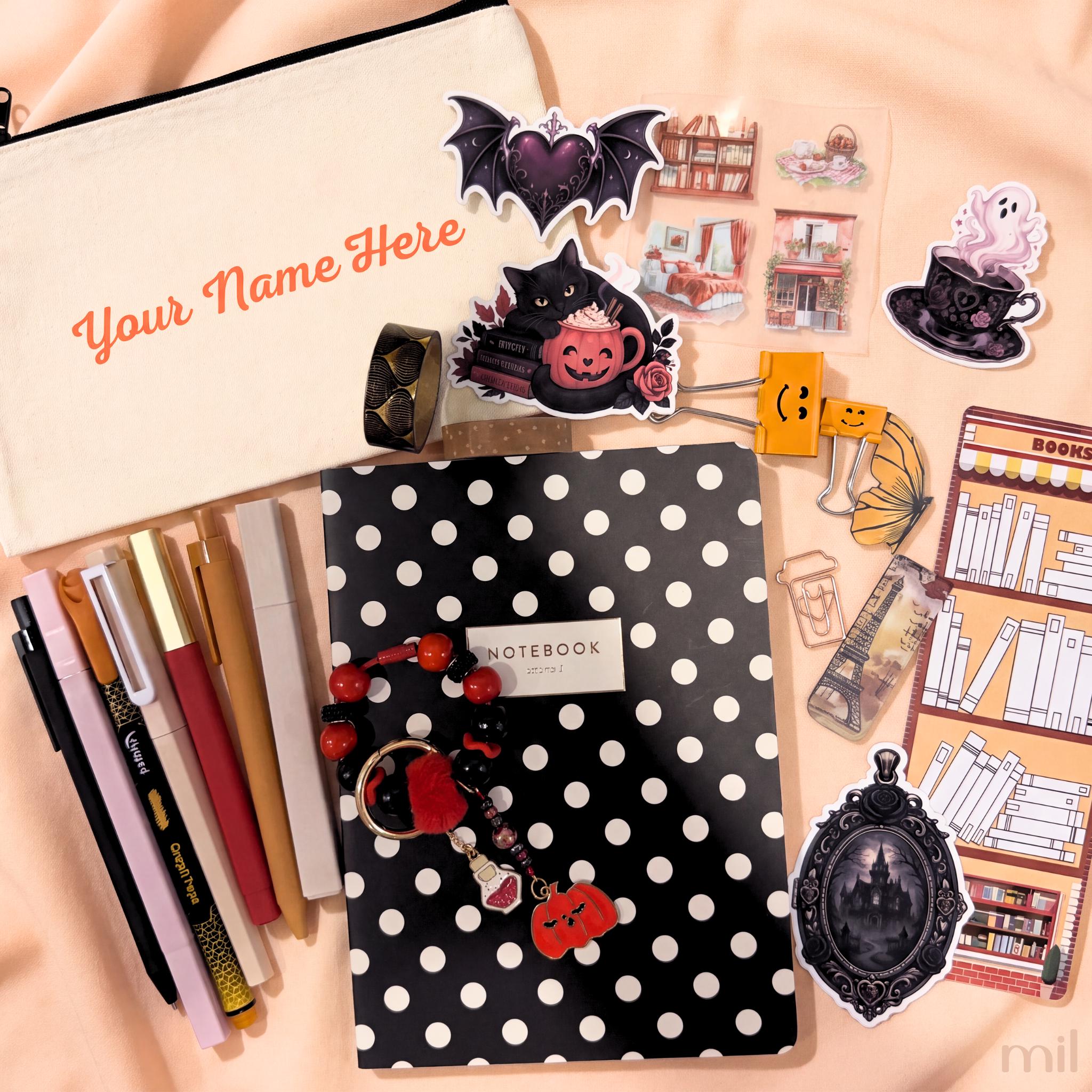 A styled flat-lay of stationery and desk accessories on a peach fabric background, including a cream zip pouch with orange text, a black-and-white polka dot notebook, pens, stickers, bookmarks, and small decorative items.