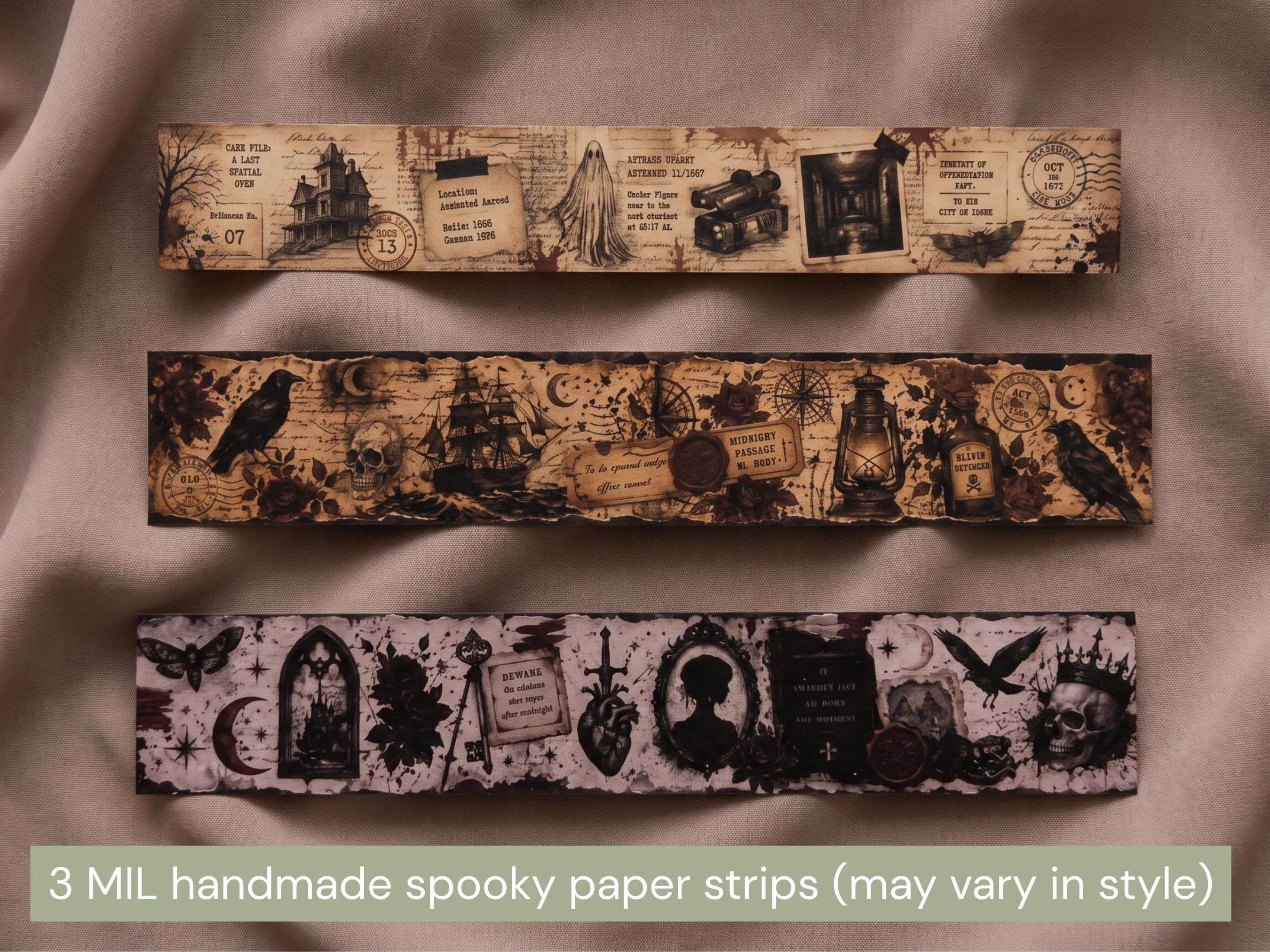 Three horizontal strips of handmade spooky paper garland displayed on a draped beige fabric background. The top strip features a haunted house and vintage postmark theme, the middle strip shows a raven and lantern motif, and the bottom strip displays gothic arches, a skull, and a heart.