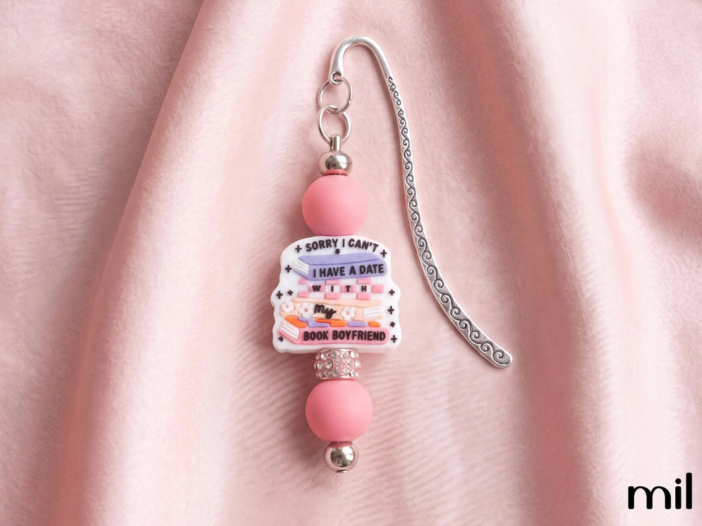 A pink and silver beaded bookmark with a central charm that reads 'SORRY I CAN'T I HAVE A DATE WITH BOYFRIEND' on a soft pink fabric background.