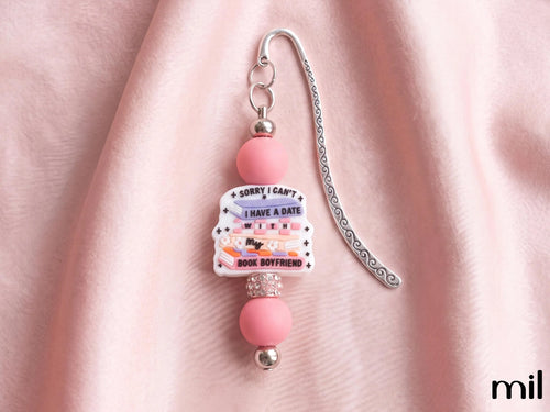 A pink and silver beaded bookmark with a central charm that reads 'SORRY I CAN'T I HAVE A DATE WITH BOYFRIEND' on a soft pink fabric background.