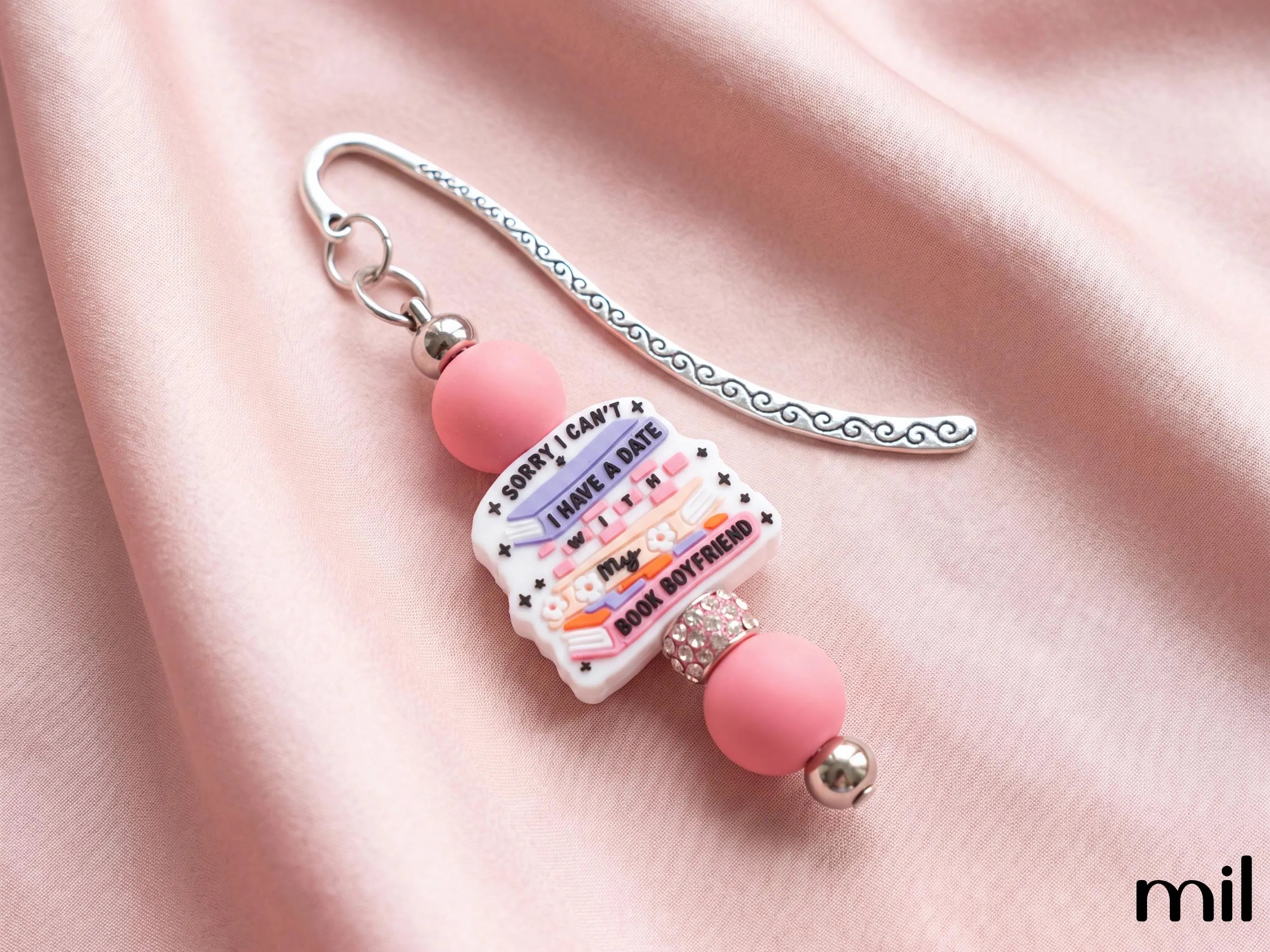 A pink and silver beaded bookmark with a decorative silver wire loop and a central printed card that reads 'Sorry I can't I have a Date with my Book Boyfriend,' displayed on a draped pink satin fabric background.