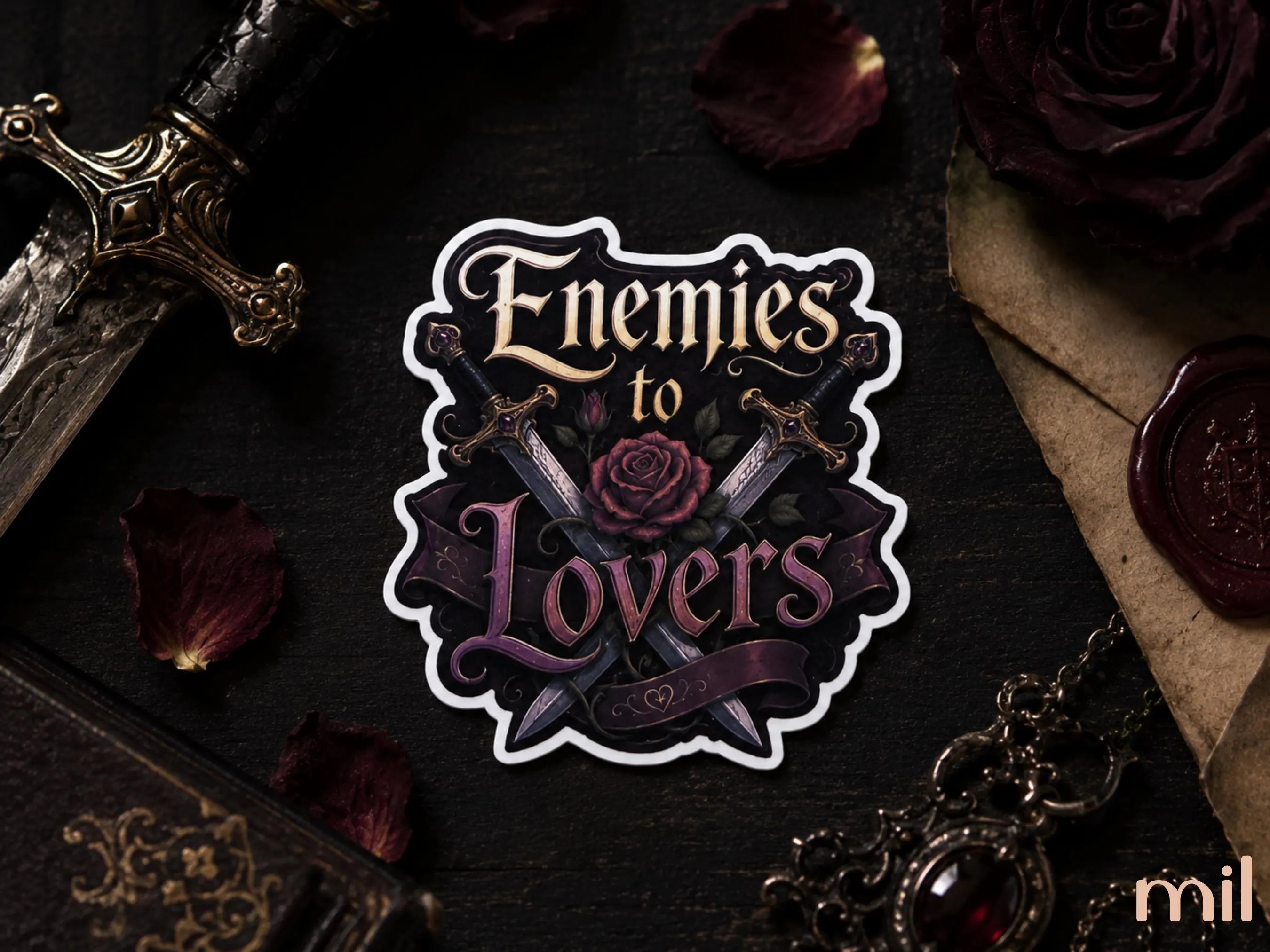 A die-cut sticker featuring the gothic phrase 'Enemies to Lovers' with crossed swords and a rose, displayed on a dark textured background with vintage props including a dagger, dried rose petals, an old book, and a wax seal.