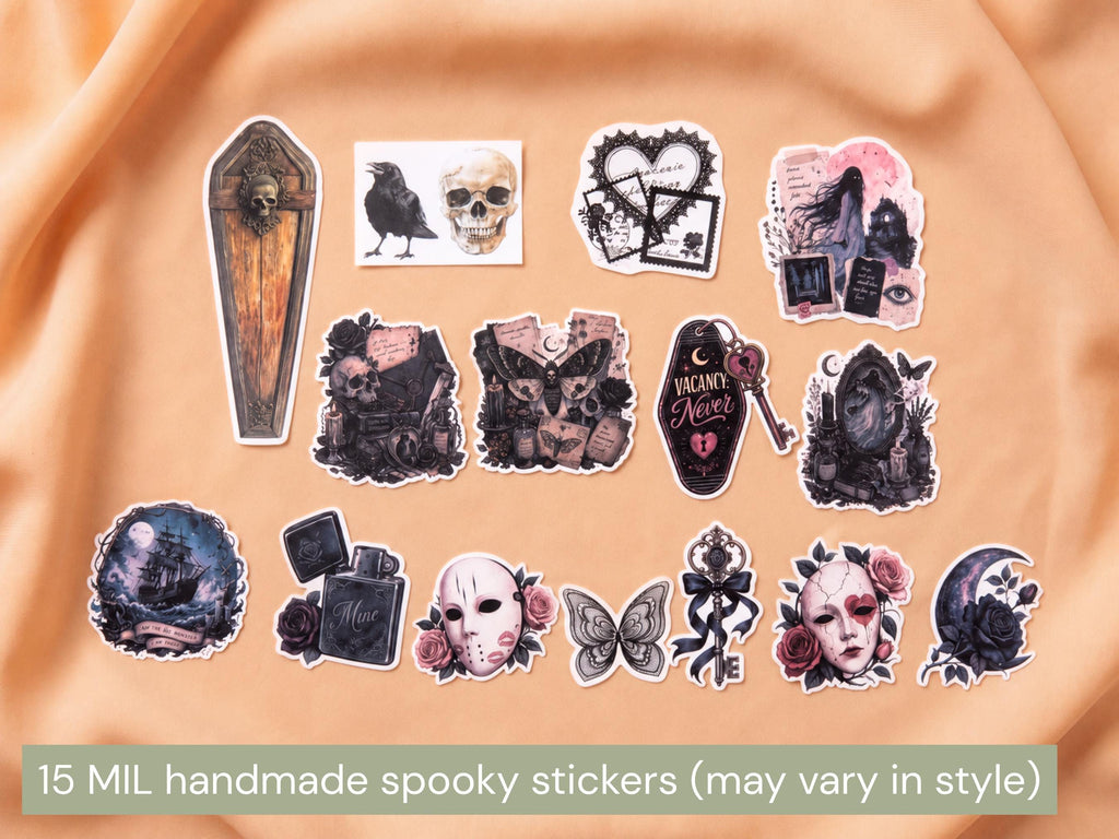 A set of 15 handmade spooky-themed stickers arranged on a peach fabric background. The stickers feature gothic designs including a coffin with a skull, a raven and skull, a broken heart, a pink gothic portrait, a key with 'You Are Not' text, a dark gothic face, a haunted house, a mask with roses, a butterfly, and a crescent moon with roses.
