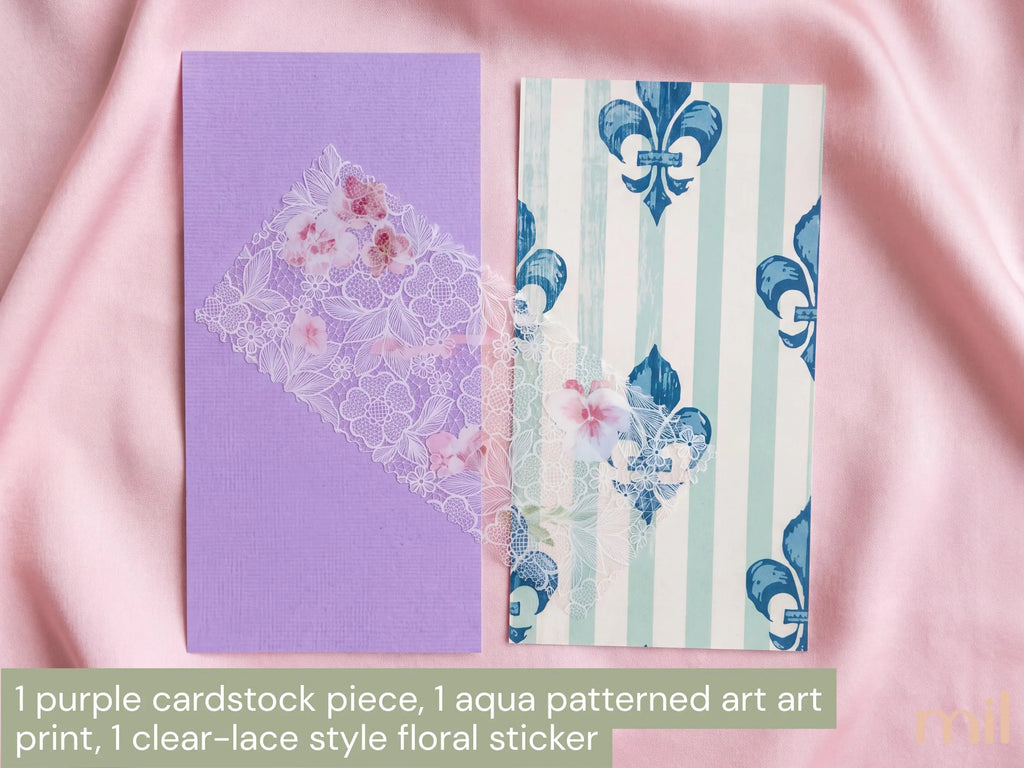 Two decorative cardstock pieces and a floral sticker displayed on pink satin fabric. One cardstock is solid lavender purple, and the other has a vertical aqua and white striped pattern with blue fleur-de-lis motifs.