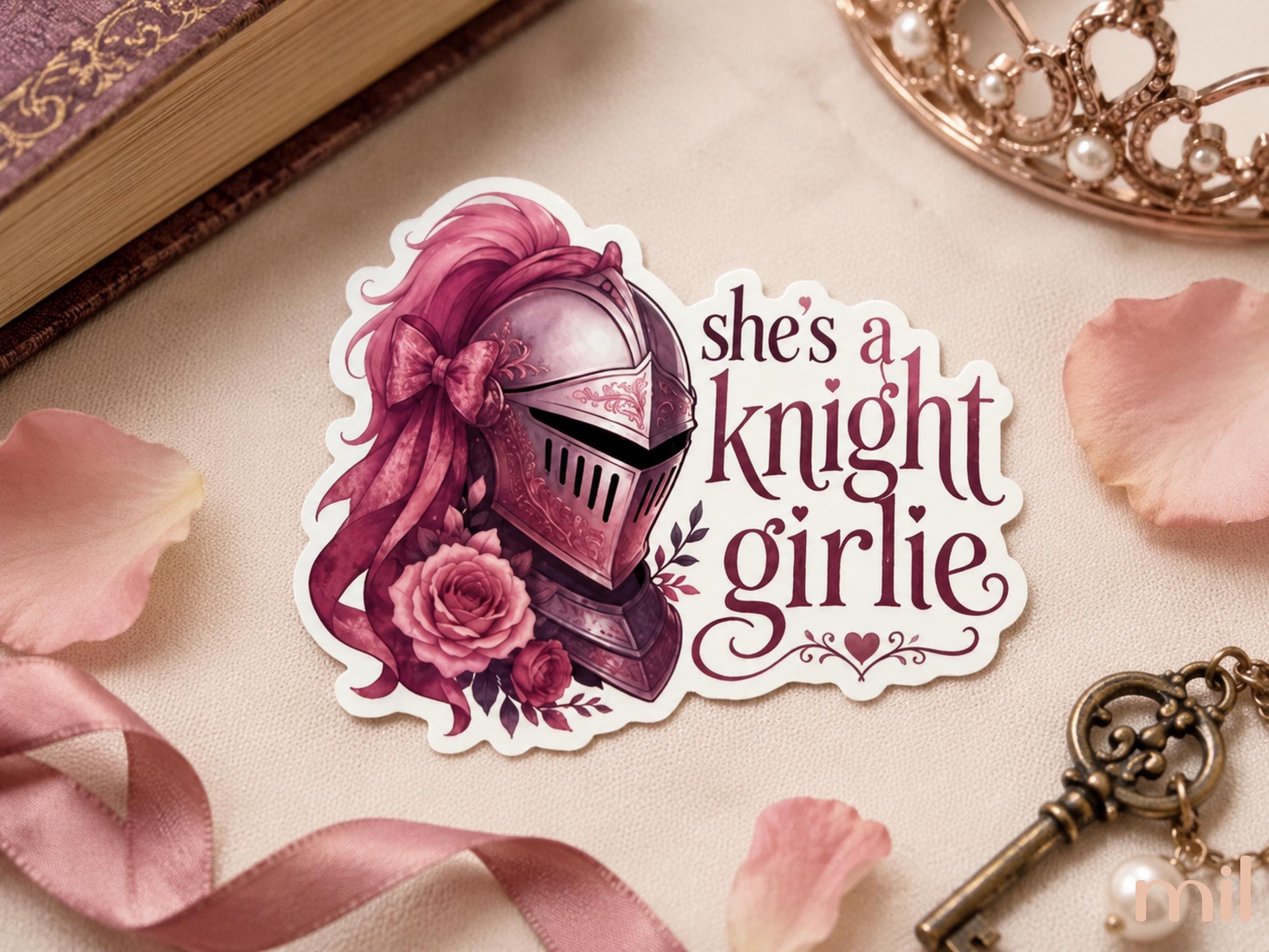 A die-cut sticker featuring an illustration of a pink-haired knight in armor with roses and the text 'she's a knight girlie', displayed on a beige marble surface with pink rose petals, a book corner, a tiara, and a vintage key.
