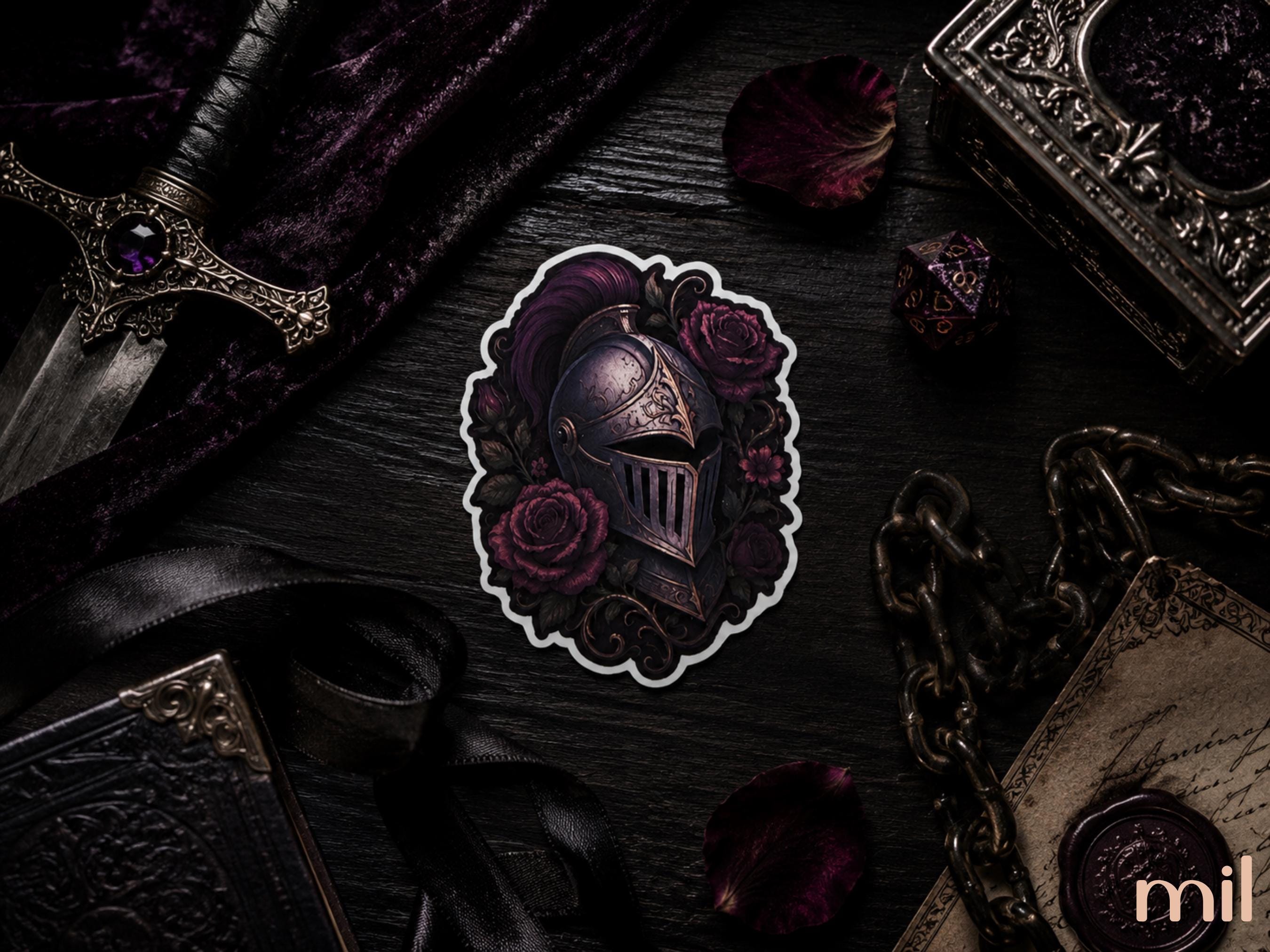 A die-cut sticker featuring a dark fantasy knight helmet surrounded by purple roses, displayed on a dark tabletop with gothic props including a dagger, velvet cloth, chain, and old book.