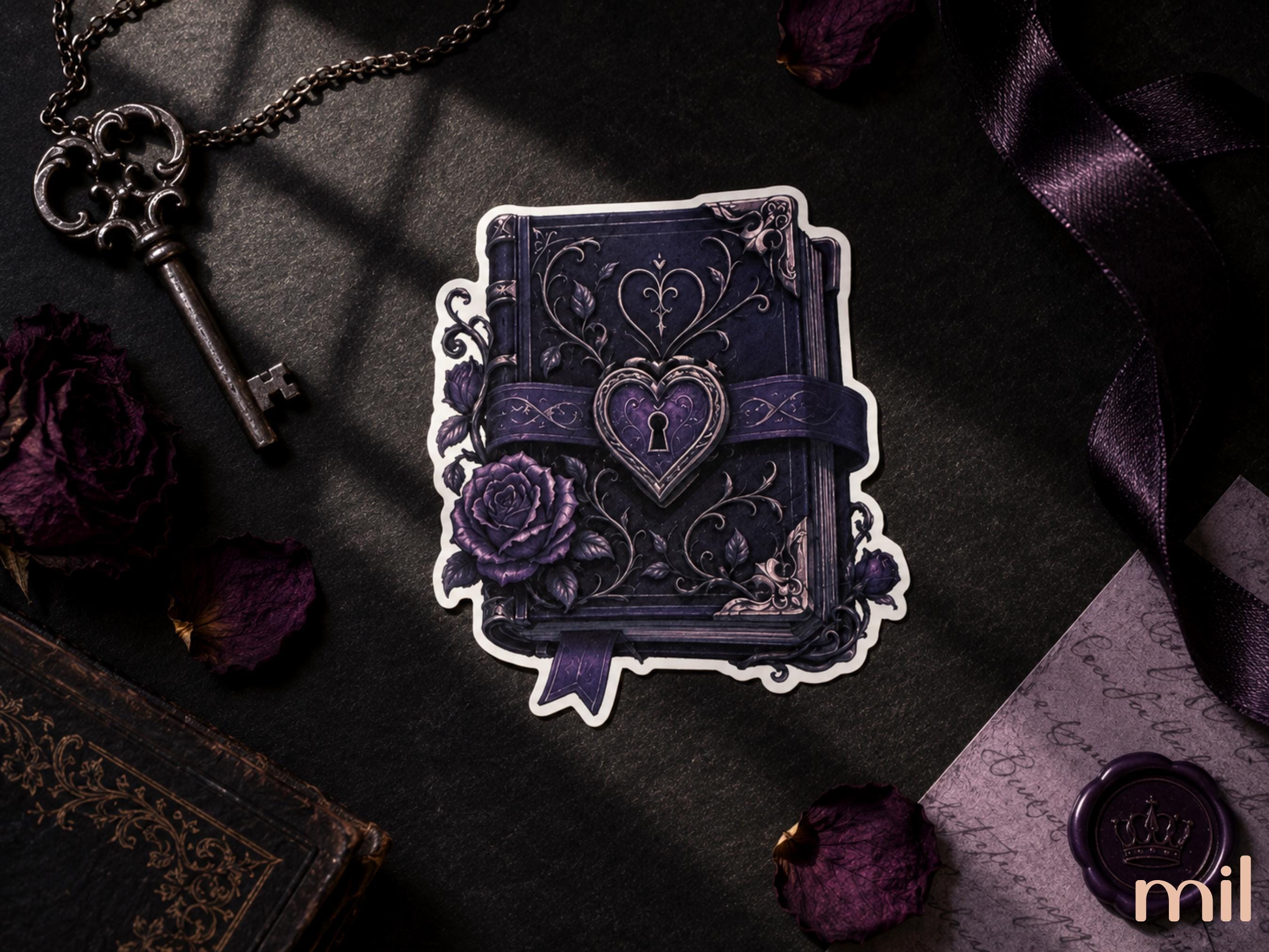 A decorative die-cut sticker featuring an ornate dark purple gothic book with a heart-shaped lock and rose illustration, shown on a dark styled flat-lay with a key, dried roses, ribbon, and wax seal.